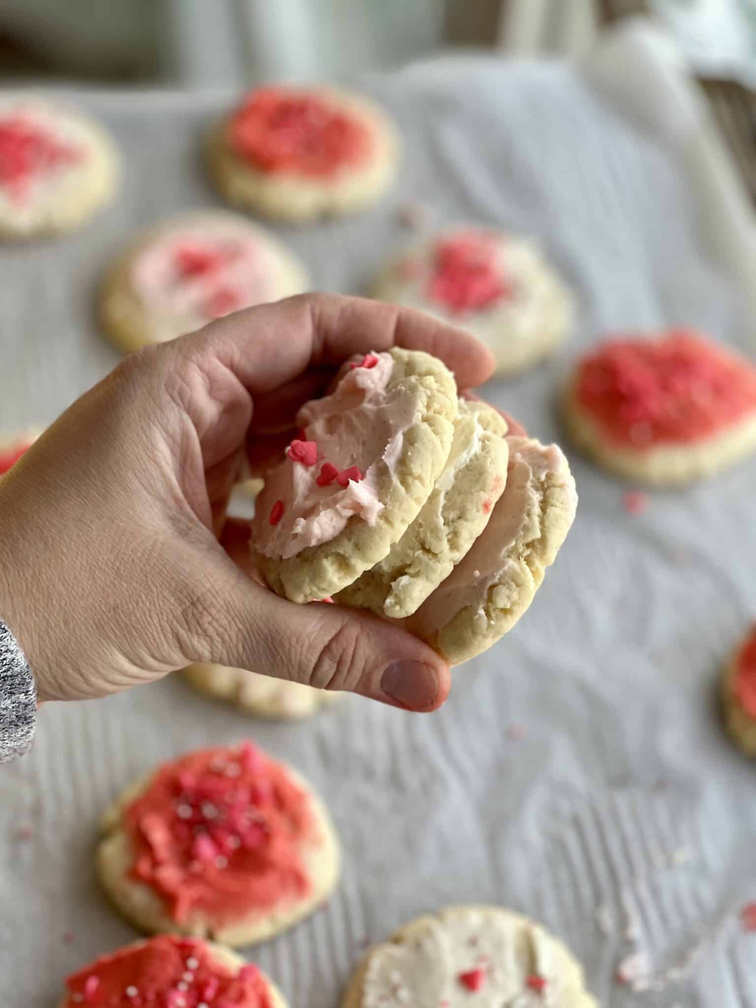 A hand holds a stack of three frosted sugar cookies.
