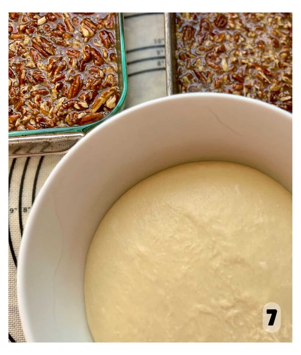 A bowl of dough is rising next to a tray of sticky pecan mixture.