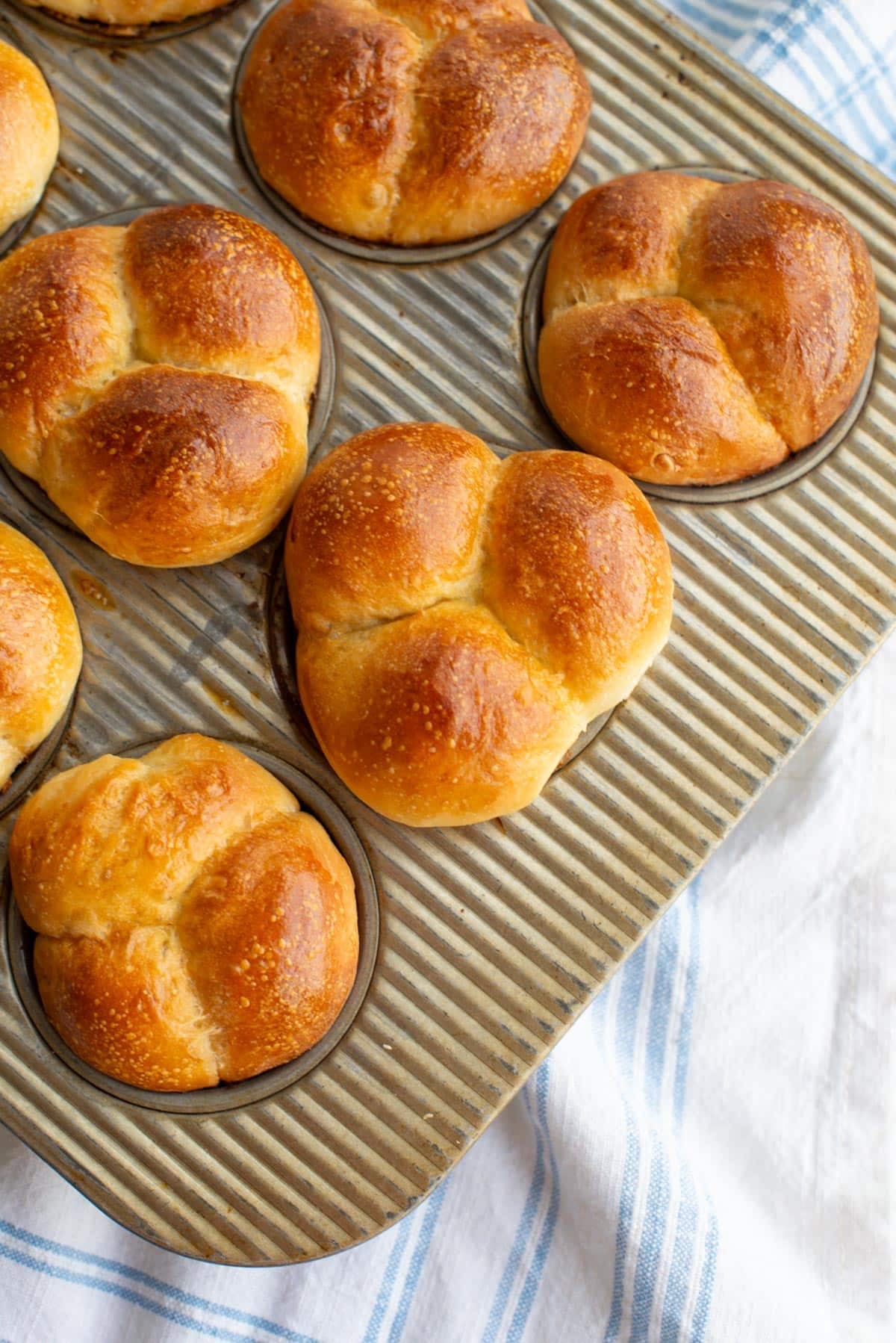 Cloverleaf rolls are golden brown and sit in a muffin tin.