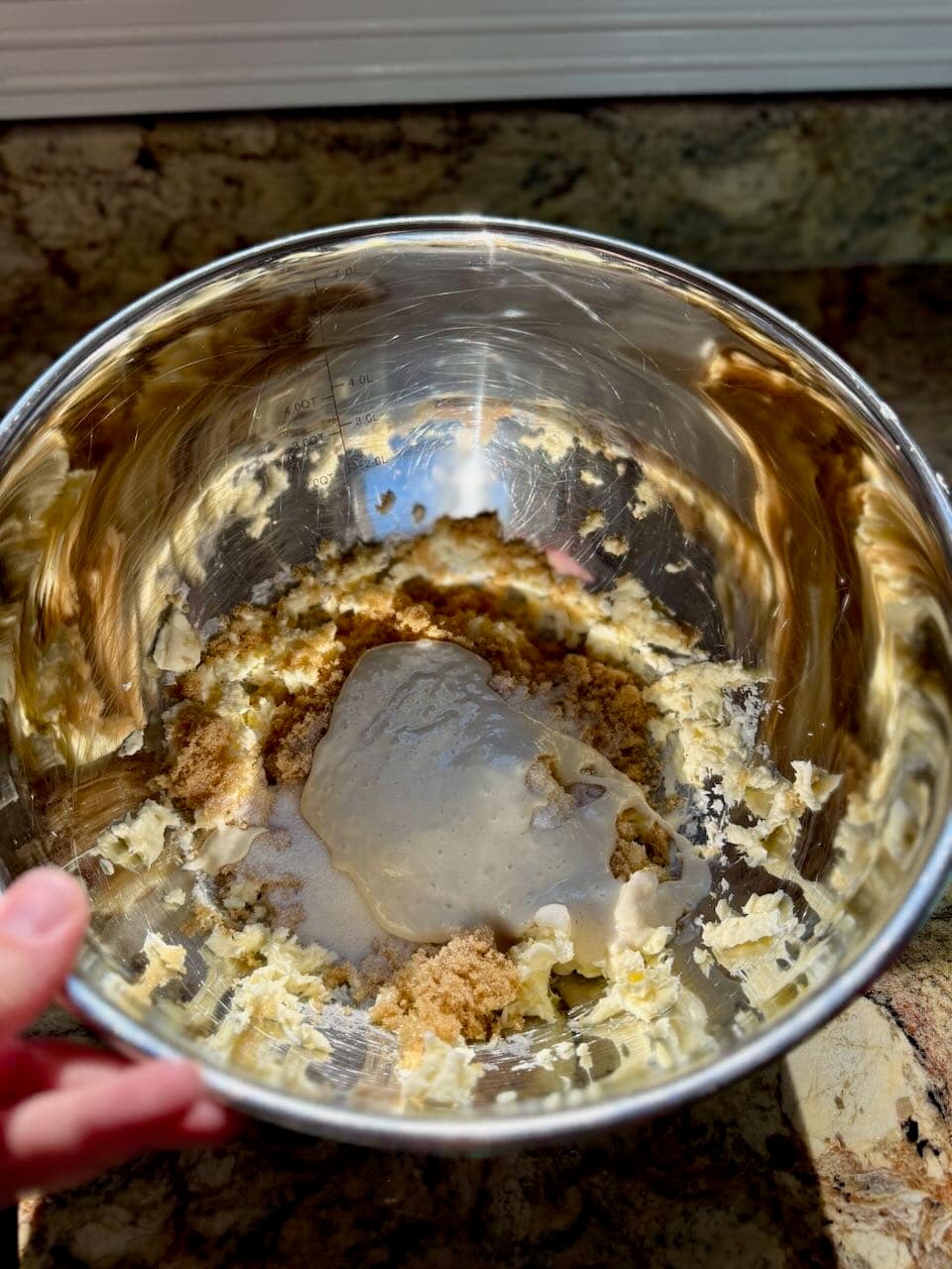 A mixing bowl with butter, brown sugar, granulated sugar, and sourdough discard being creamed together for cookie dough.