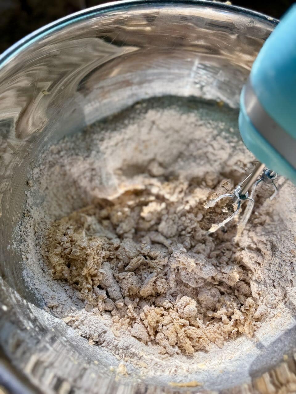 Cookie dough forming in a mixing bowl as flour and oat mixture are combined with a hand mixer.