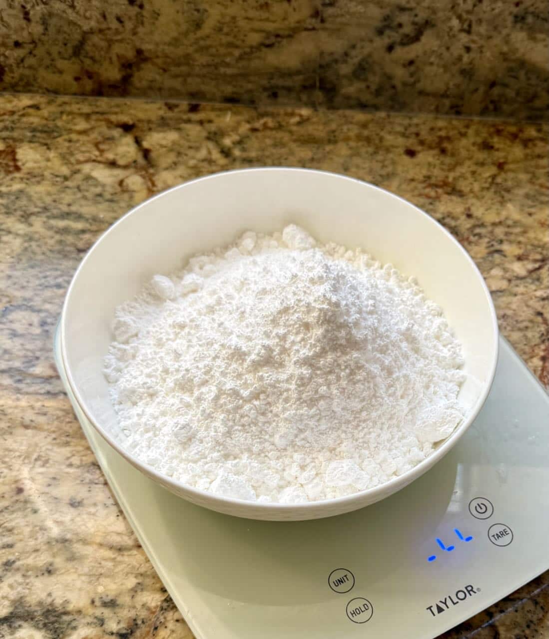 A bowl of powdered sugar sits on a kitchen scale.
