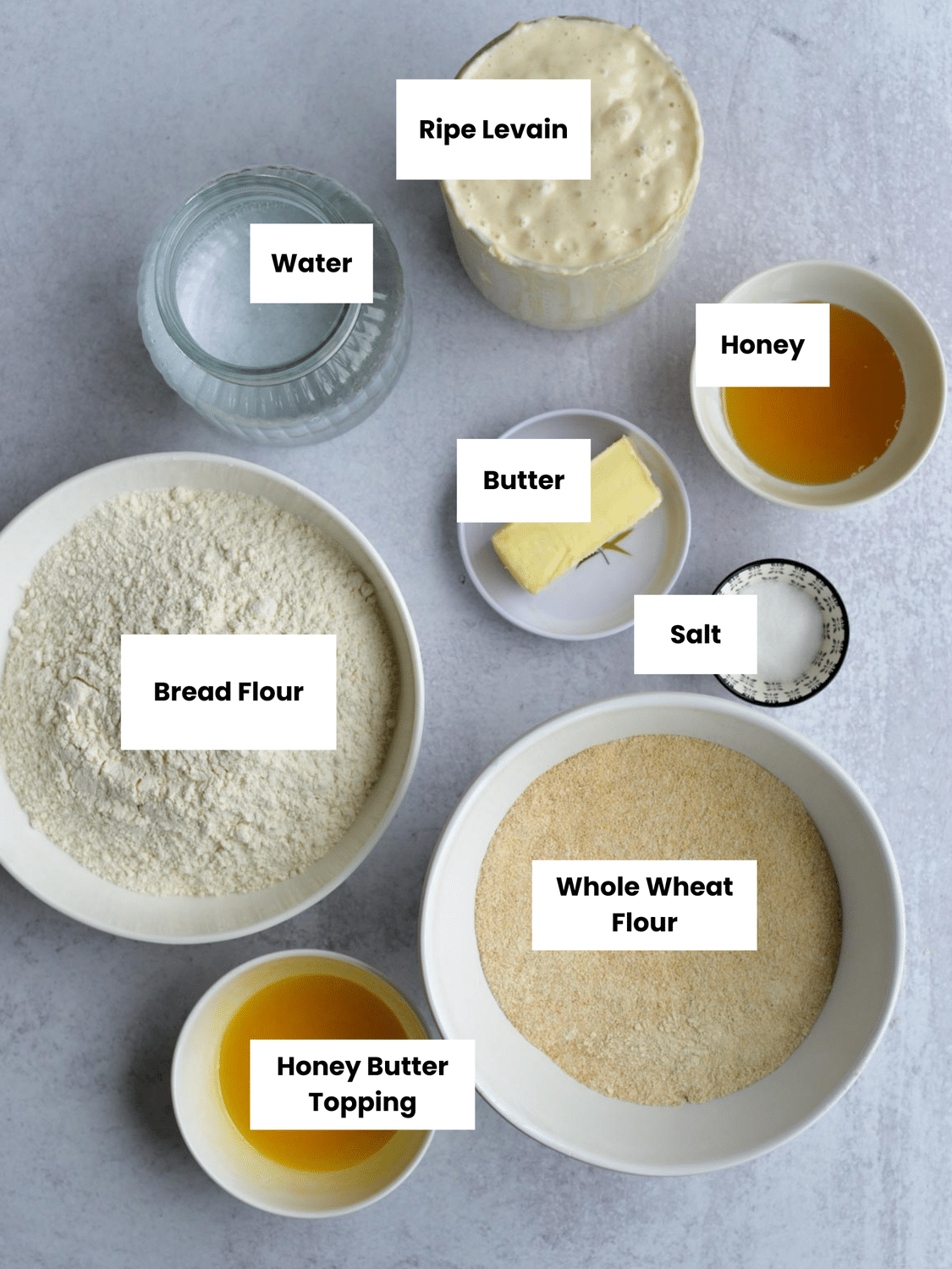 Ingredients on a kitchen counter include ripe levain, water, honey, butter, salt, bread flour, whole wheat flour, and honey butter topping.