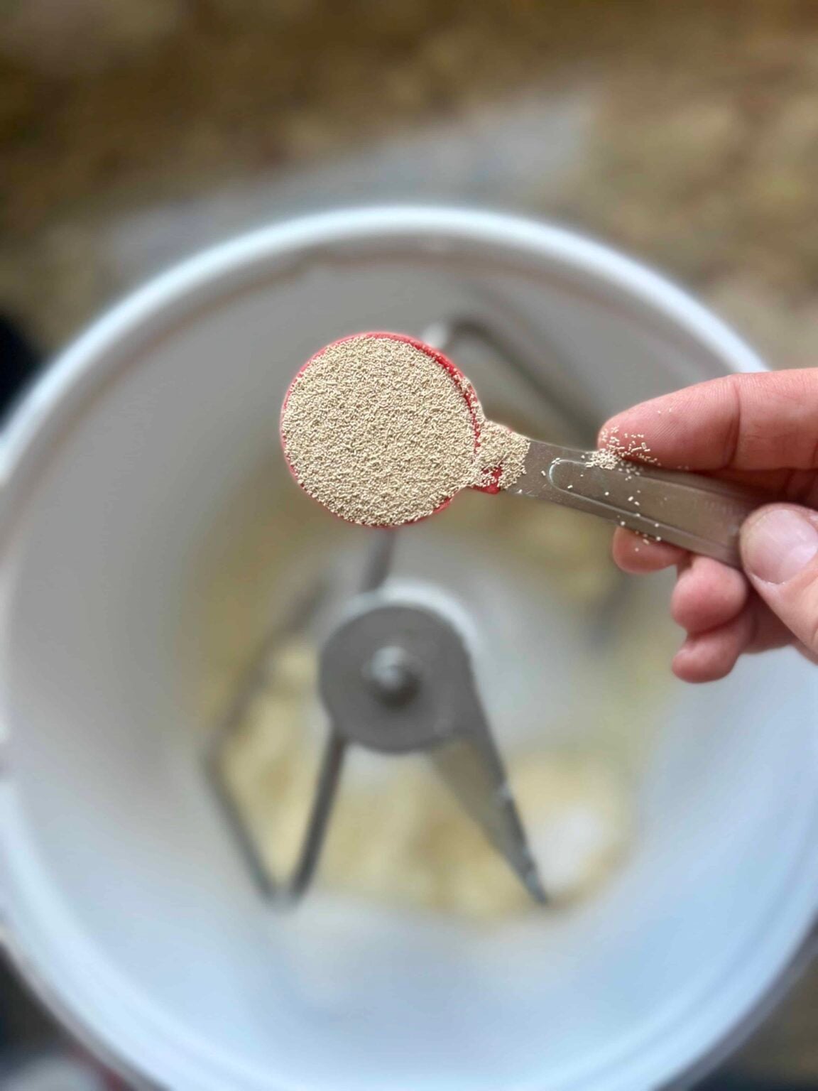 A tablespoon measure of yeast is held over a stand mixer.