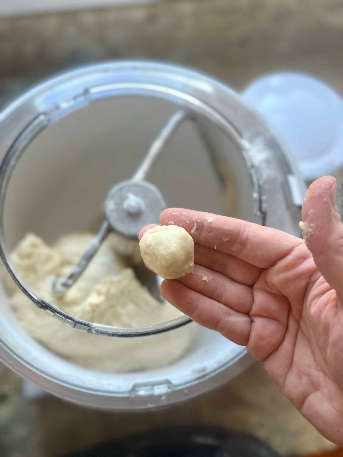 A ball of dough is held between fingers over a stand mixer where the dough has pulled away from the sides.