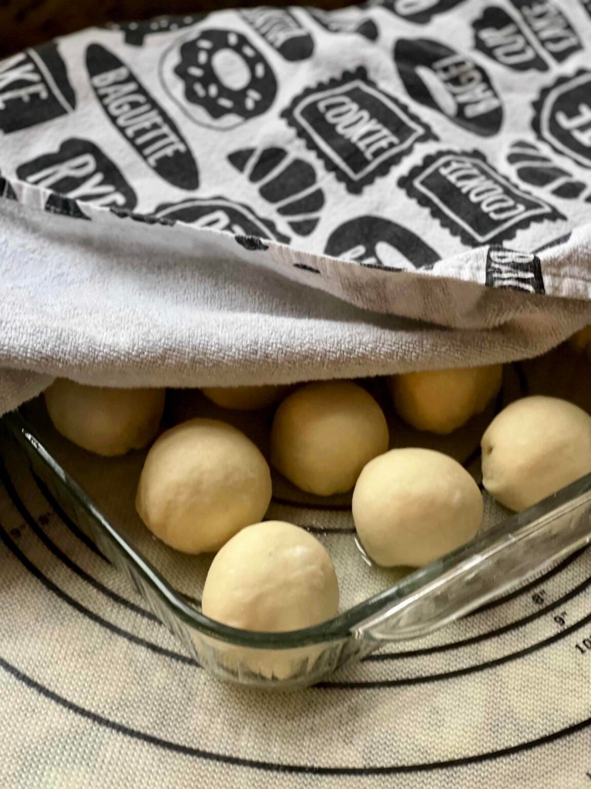 Rolls rising in a glass pan are covered with a kitchen towel.