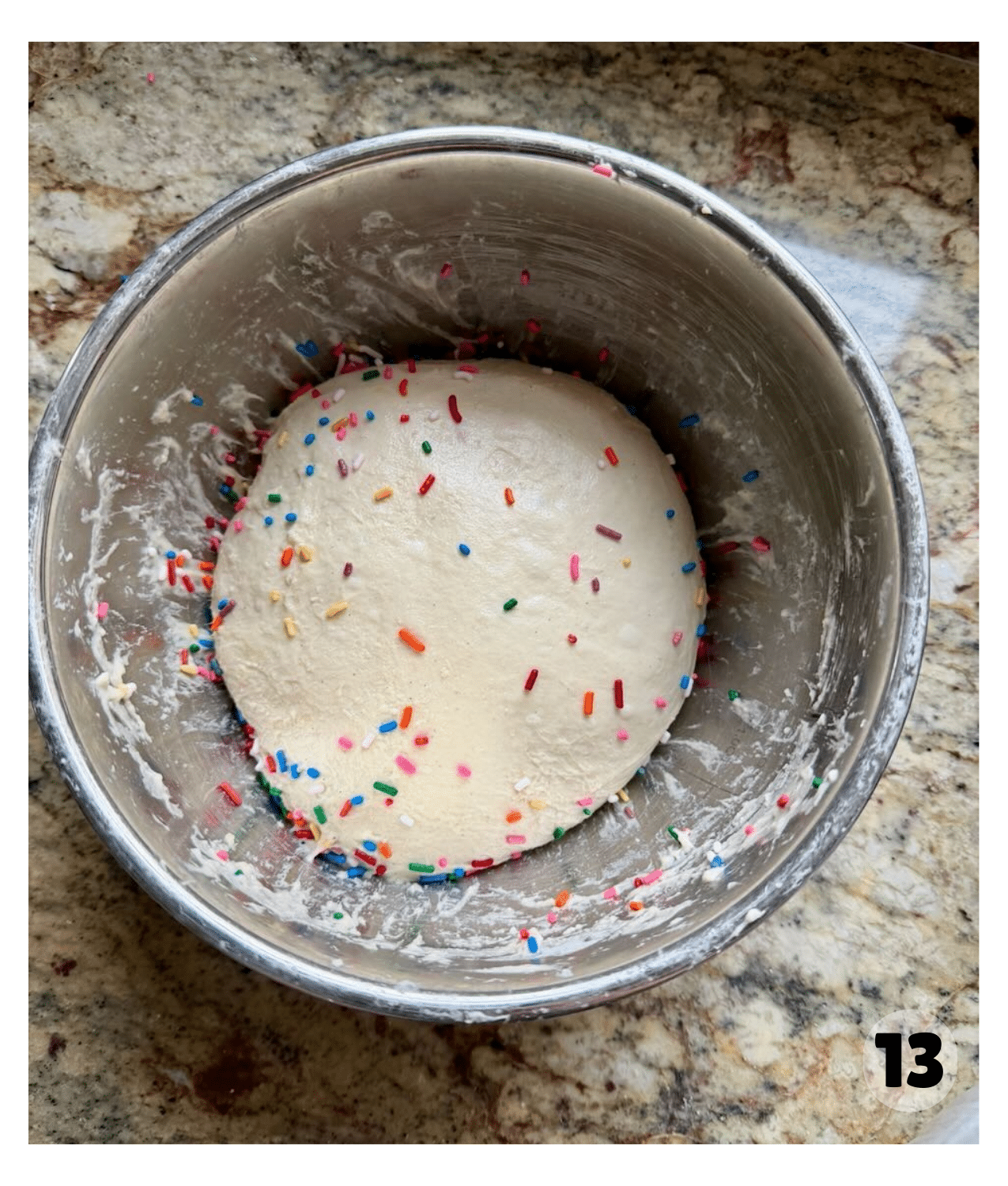 Funfetti sourdough dough resting in a metal bowl, dotted with rainbow sprinkles after the first round of stretch and folds.