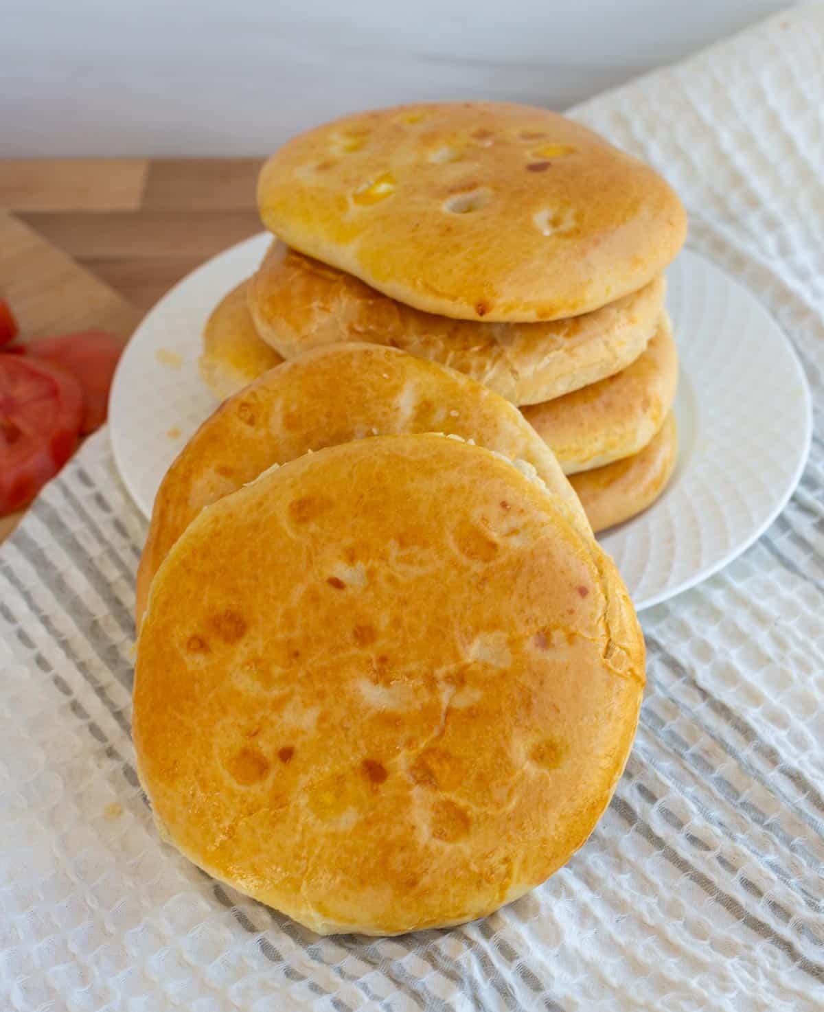 A plate contains four pide breads stacked on a plate next to two other rolls.