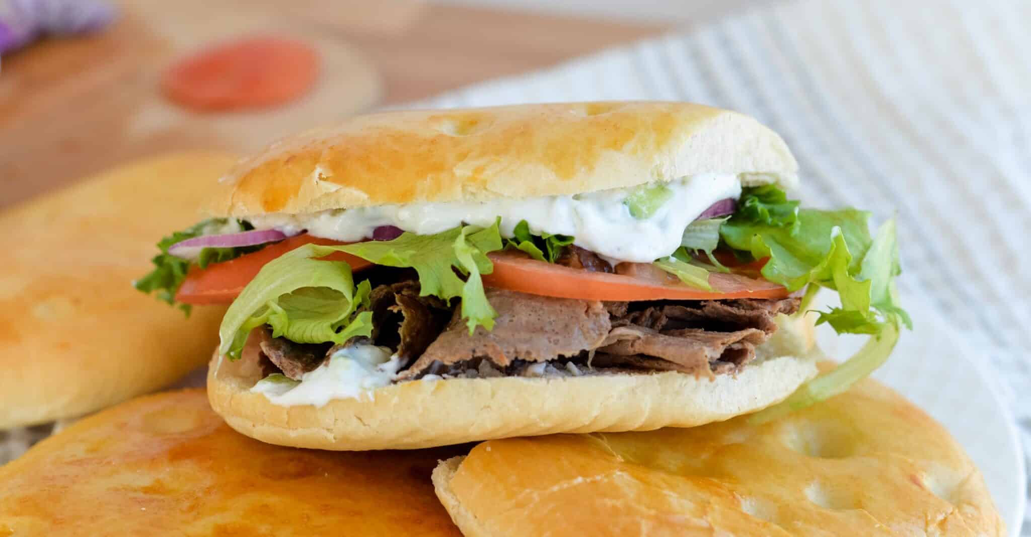 A Döner Kebab on homemade sourdough discard pide bread sits on top of a pile of unsliced bread.