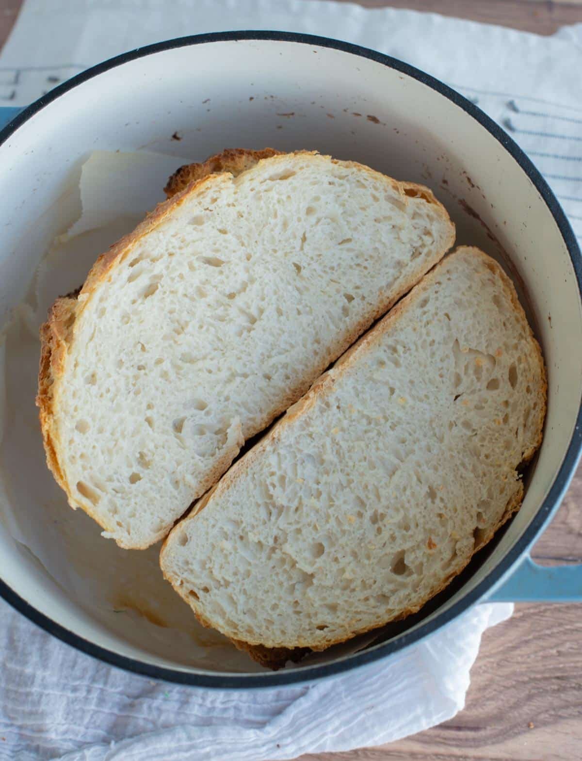 Two halves of a crusty loaf of bread sit with bottoms touching in a Dutch oven. 