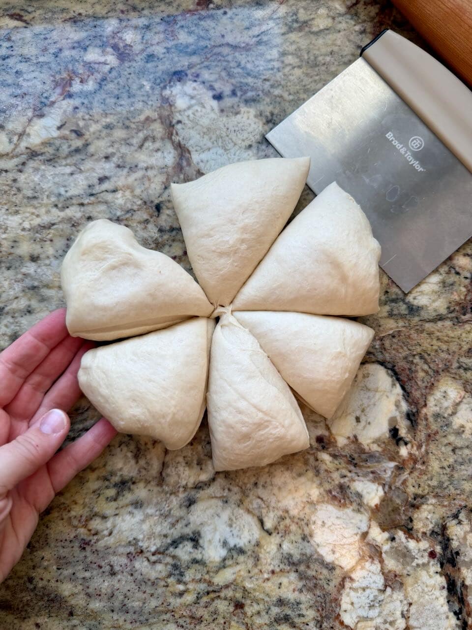 A bench knife sits next to dough that has been cut into six pieces.