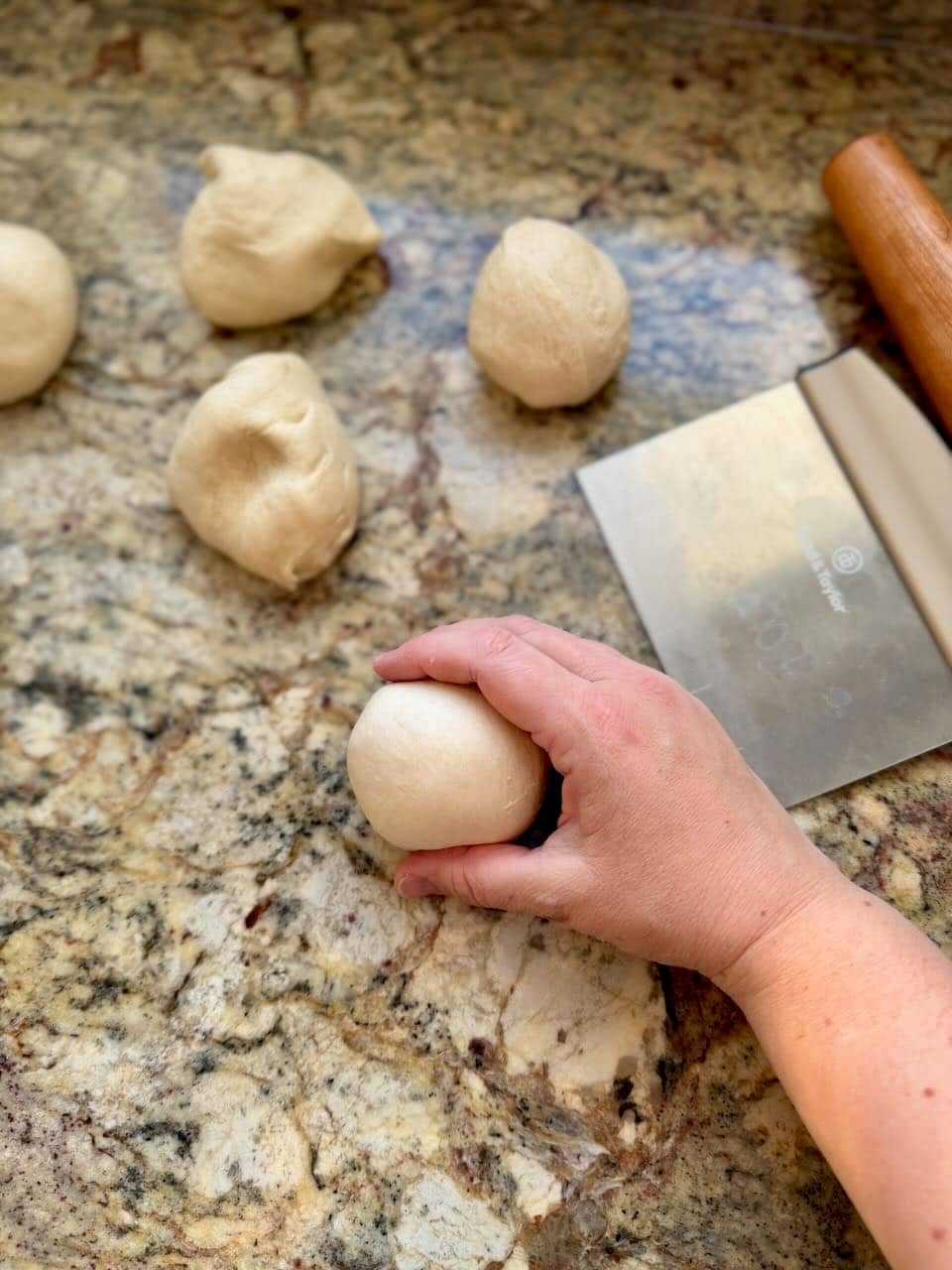A hand rolls a ball of dough on the counter.