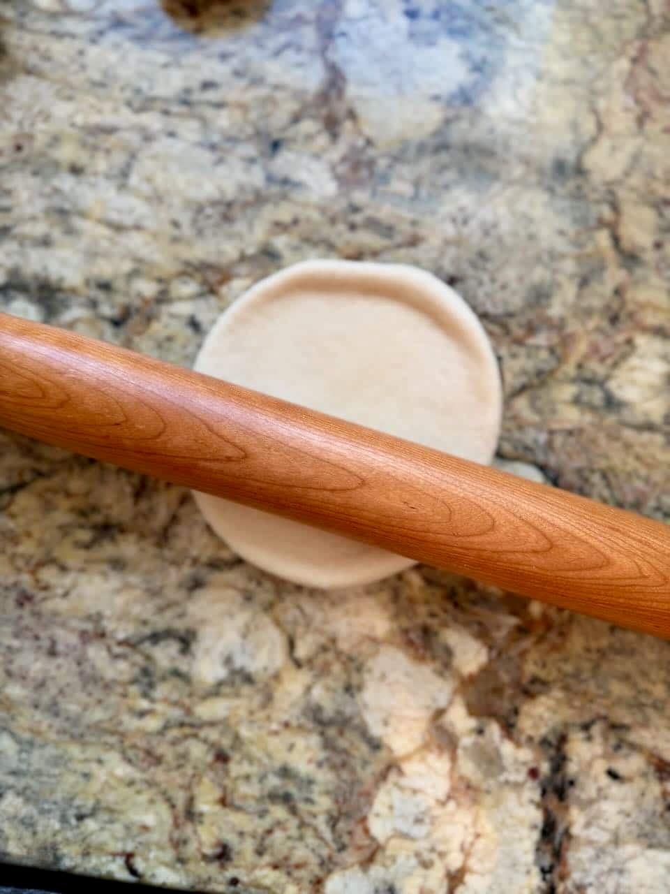 A rolling pin flattens a circle of dough.