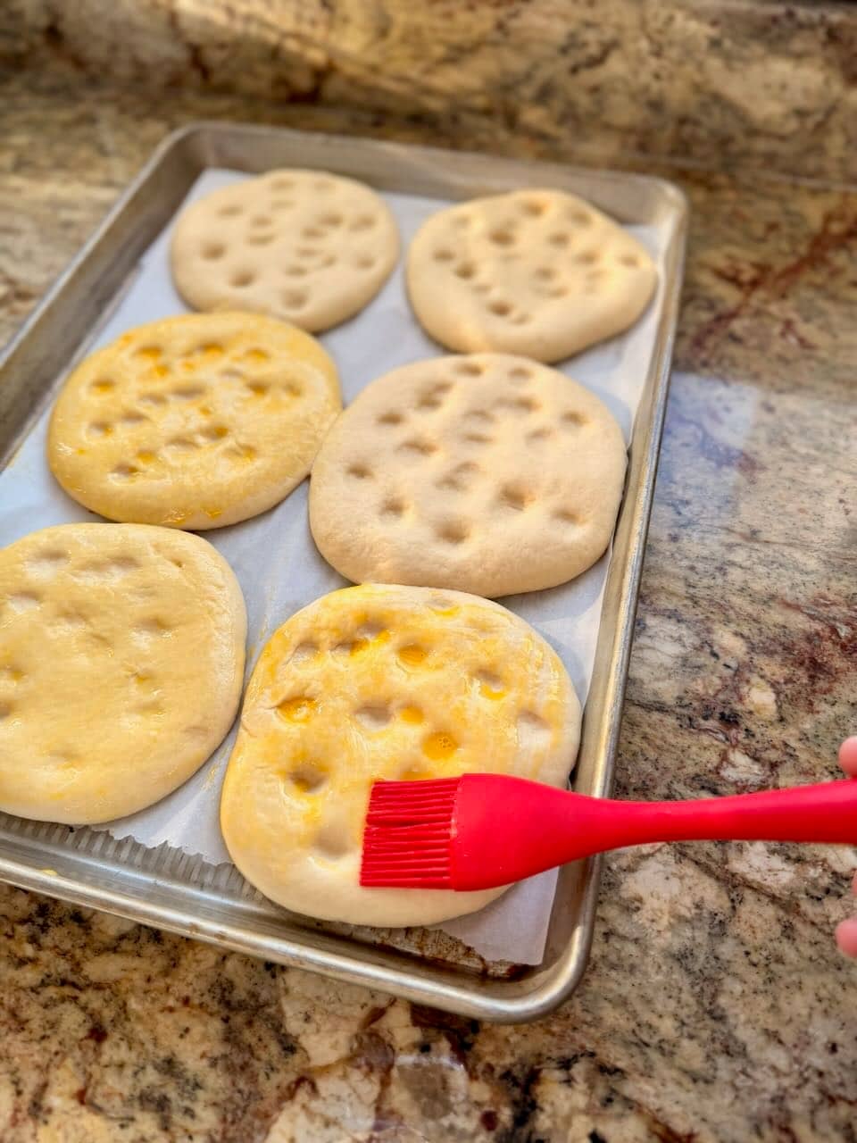Pide bread is dimpled and an egg wash is being brushed onto them.