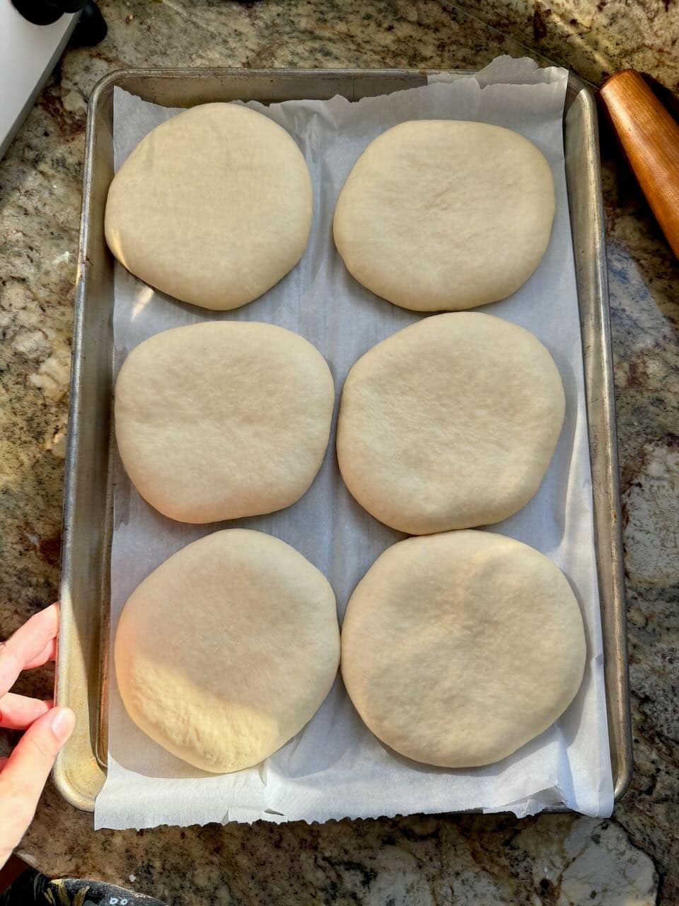 Six pieces of dough are risen and puffed sitting on a parchment lined baking sheet.