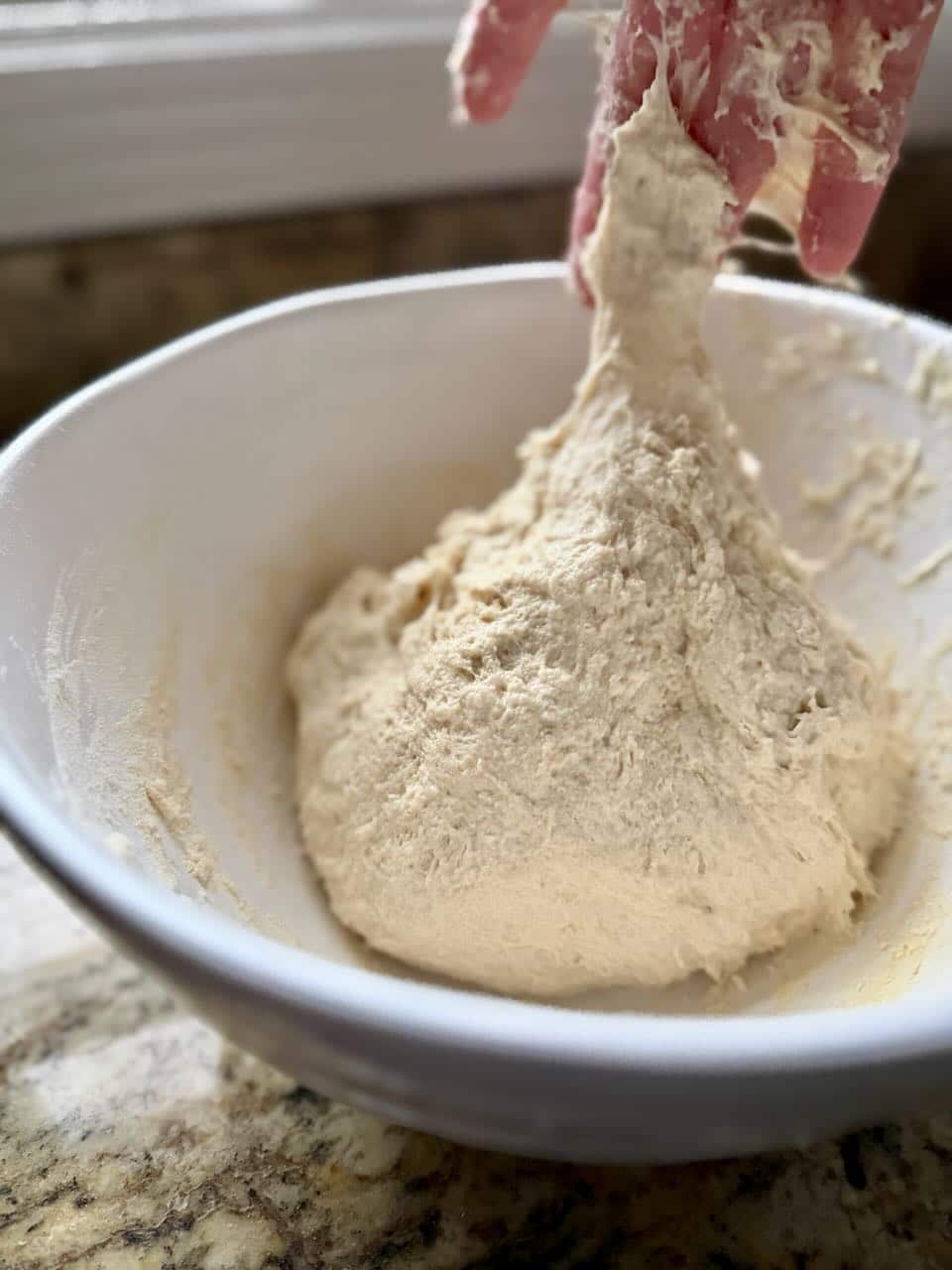 A hand mixes dough in a mixing bowl.