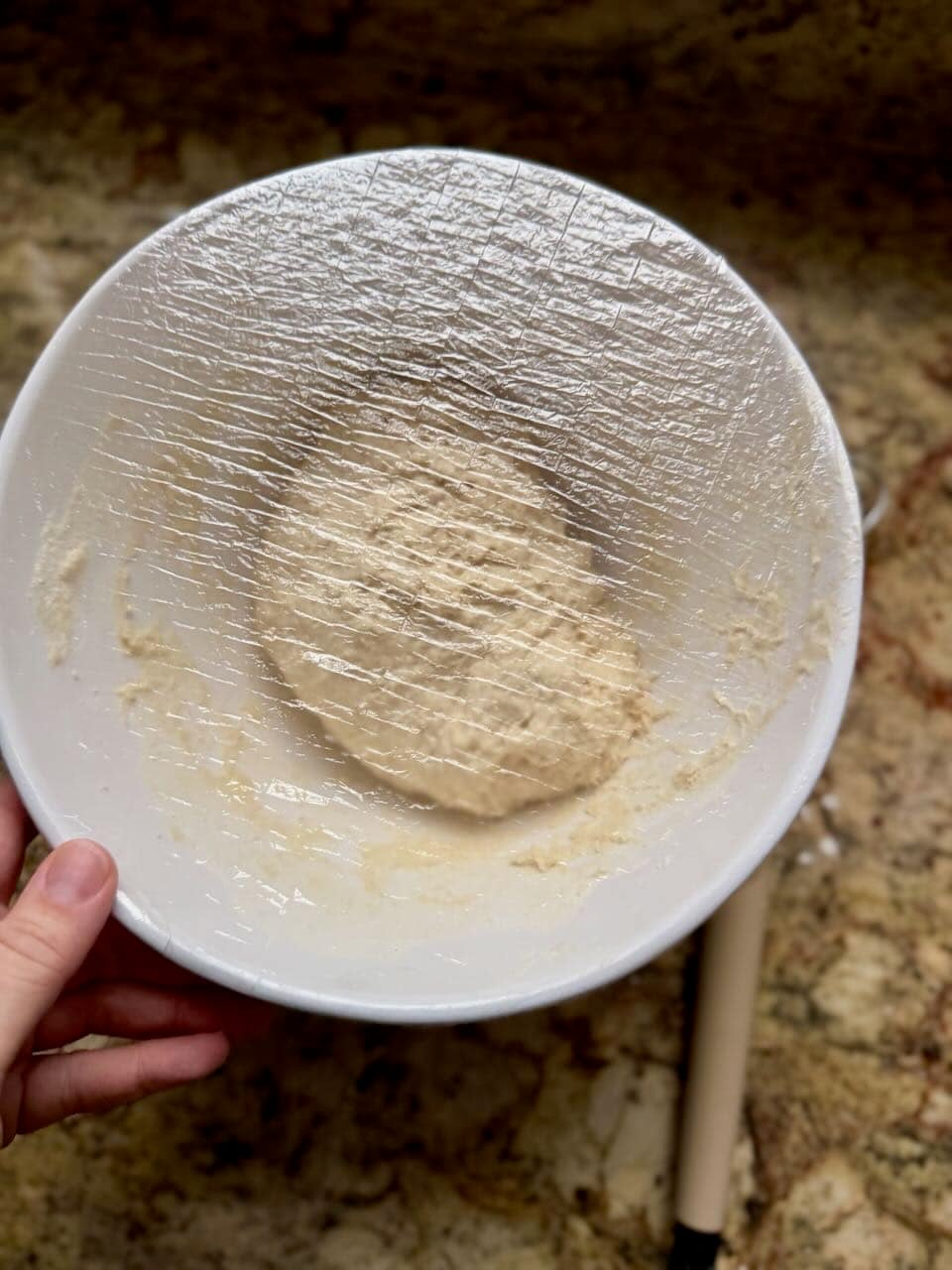 A ball of dough sits in a mixing bowl covered with plastic wrap.