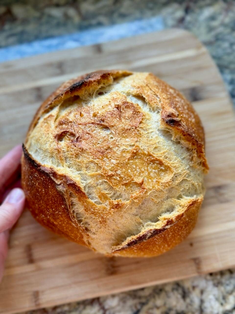 A golden brown loaf of bread sits on a cutting board.