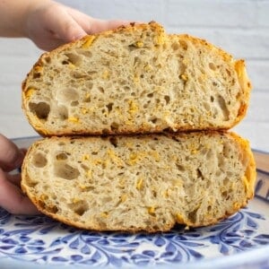 Italian herb and cheese sourdough loaf sliced in half on a platter.