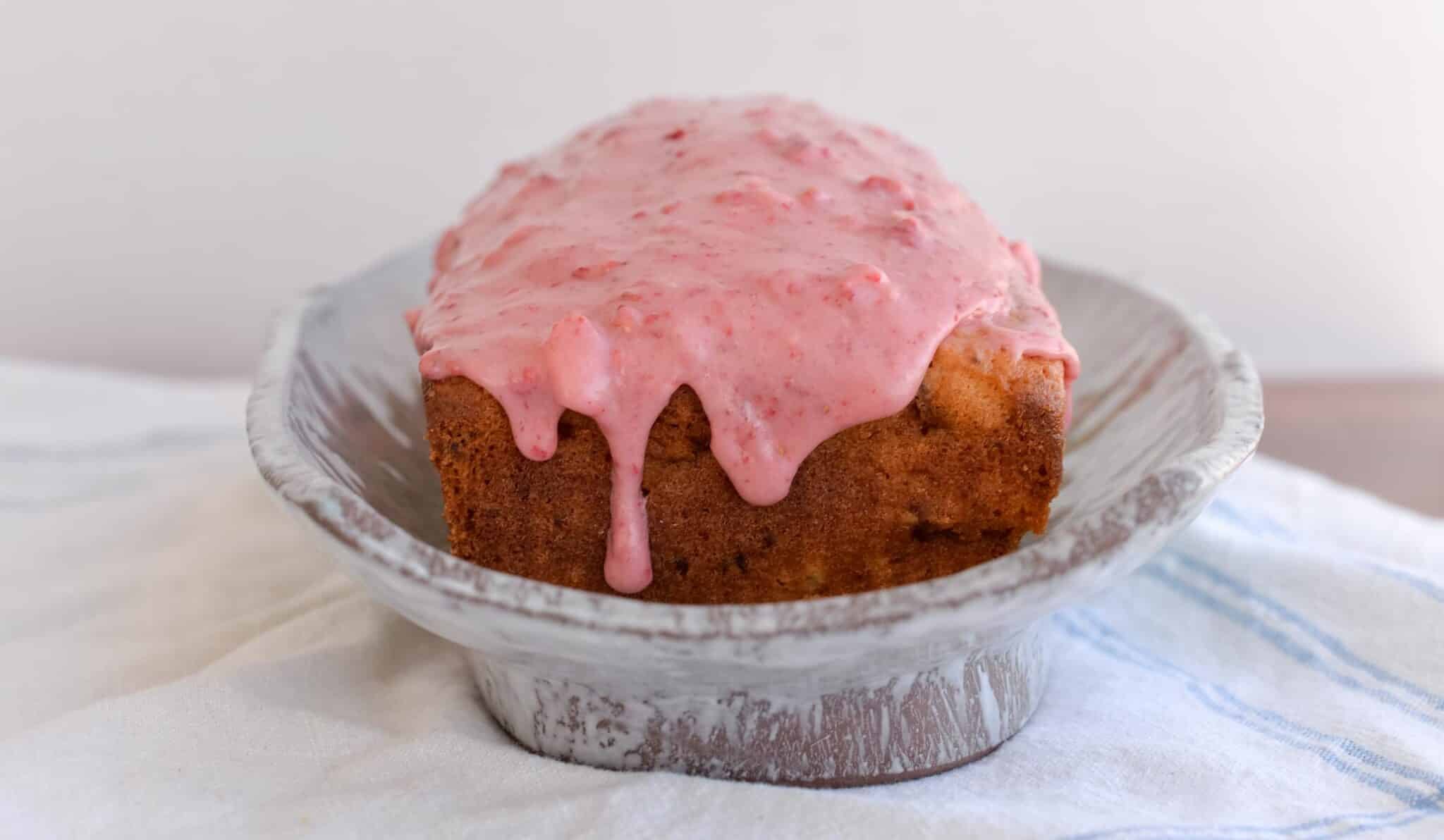 Sourdough discard strawberry bread topped with thick pink strawberry glaze dripping down the sides, displayed in a rustic ceramic dish.