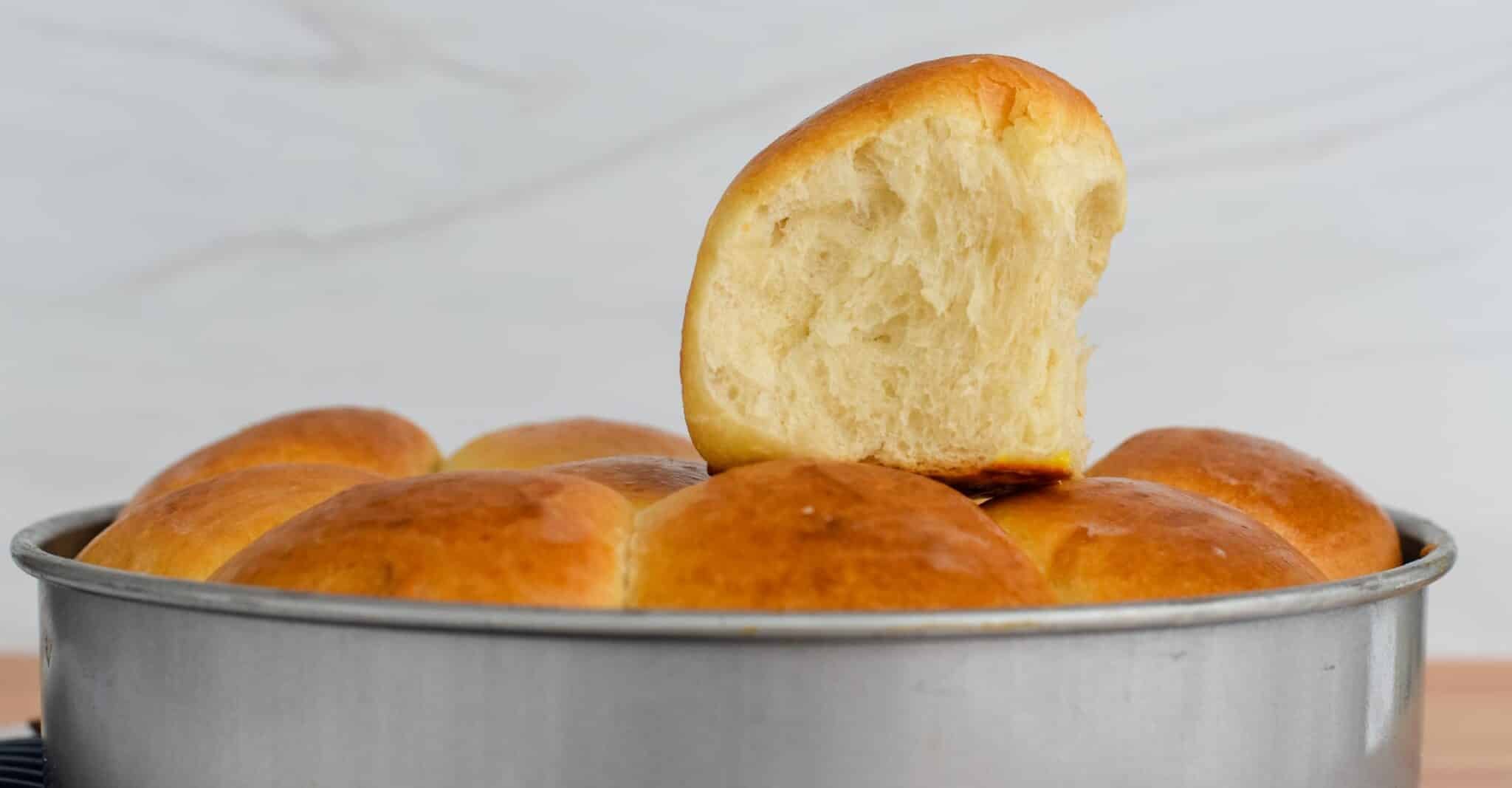 Golden sourdough brioche rolls baked in a round pan with one roll cut open on top showing the soft, fluffy interior.