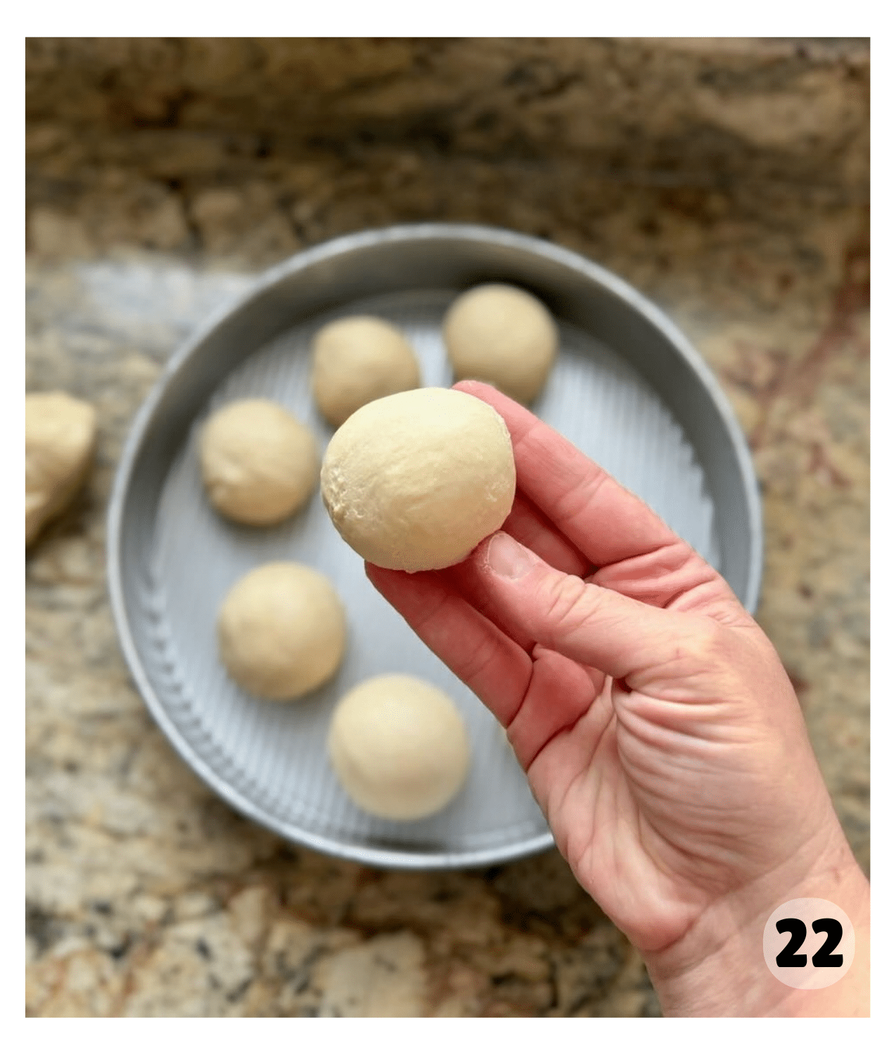 A shaped roll is held up over a round pan of shaped rolls.